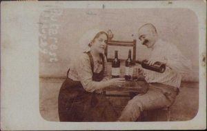 Kurt Katalin și Rudi, bănățeni din Sânnicolau Mare, la un pahar de vin românesc (se disting numele vinurilor pe etichetele sticlelor) la București, cu papagalul pe marginea scaunului, 1914